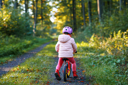 Child riding balance bike. Kids on bicycle in sunny forest. Little girl enjoying to ride glider bike on warm day. Preschooler learning to balance on run bicycle in safe helmet. Sport activityの写真素材
