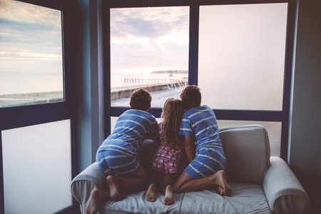 Three children watching sunrise on terrace or balcony. Two kids boys and preschool girl watch sun on horizon. Happy children relaxing near beach, family enjoying beautiful view.の写真素材