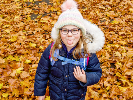 Happy school girl with a wide smile lies on a carpet of red and yellow leaves in an autumn park....