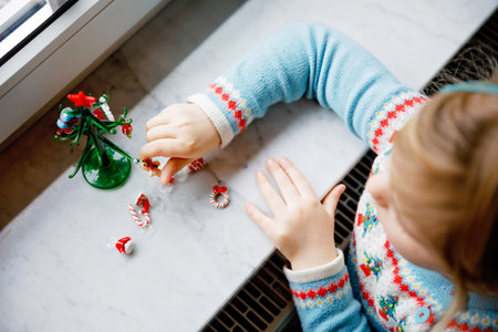Litte toddler girl sitting by window and decorating small glass Christmas tree with tiny xmas toys. Happy healthy child celebrate family traditional holiday. Adorable baby.の写真素材