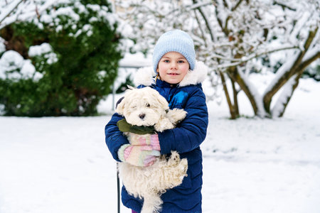 Little school girl playing with little maltese puppy outdoors in winter. Happy child and family dog having fun with snow.の写真素材