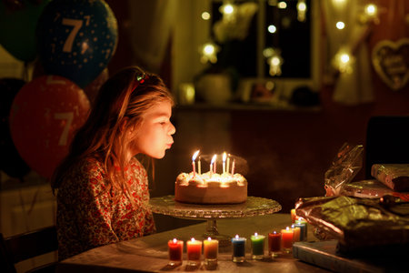 Happy little girl celebrating birthday. Cute smiling child with homemade princess cake, indoor. Happy healthy preschool kid blowing seven candles on cakeの写真素材