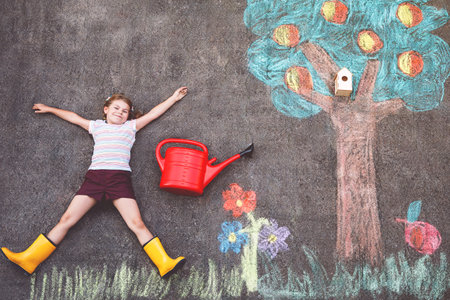 Cute little girl painting with colorful chalks apples harvest from apple tree on asphalt. Cute preschool child with having fun with chalk picture. Creative leisure for children, drawing and painting.の写真素材