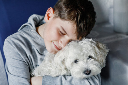Happy teenager boy and cute maltese puppy together. Handsome child holding his dog at home, hugging....