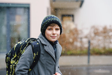 Portrait of preteen kid boy outdoors. Handsome child boy in coat and hat in winter. Schoolchild on the way to school with backpack satchel during snowの写真素材