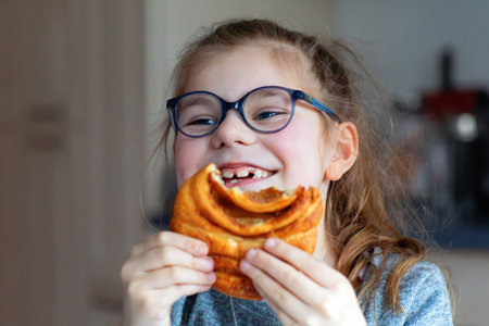 Little schoolgirl eating cinnamoon roll for school lunch. Hansdsome girl having lunch break. Unhealthy food for children.の写真素材