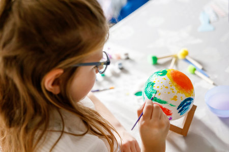Little girl painting globe or ball with colors. School child making earth globe for school project. Happy kid with eyeglasses holding brush.の写真素材