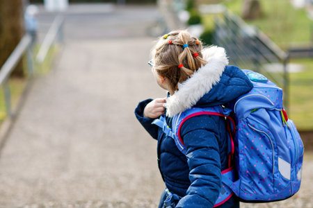 Cute little girl o the way to school. Healthy happy child with eyeglasses walking to primary school. Smiling child with schoolbag on the city street, outdoors. Back to school.の写真素材