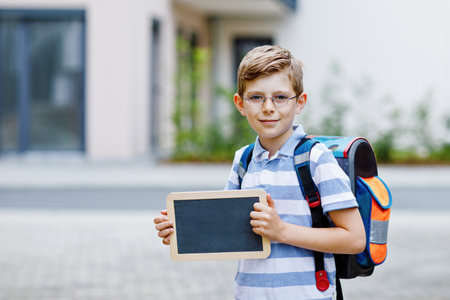 Happy little kid boy with backpack or satchel. Schoolkid on the way to school. Healthy adorable child outdoors With chalk desk for copyspace. Back to school or schools out.の写真素材
