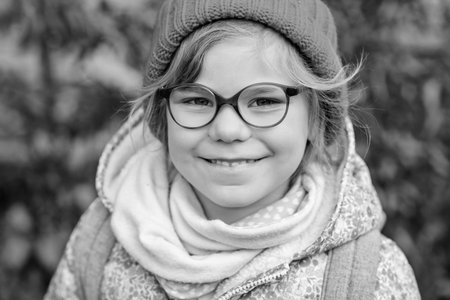 Portrait of a cute preschool girl with eye glasses and red hat outdoors. Happy funny child wearing...