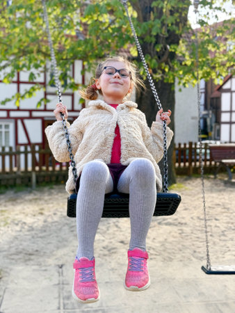 Adorable little girl having fun on a swing. Happy child on playground on sunny dayの写真素材