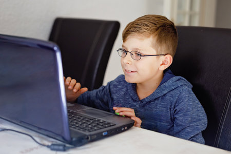 Happy healthy kid boy with glasses doing school homework at home with notebook. Interested child writing essay with helping of internet. concetrated schoolchildren concept.の写真素材