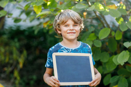 Happy little kid boy with chalk desk in hands. Healthy adorable child outdoors. Empty chalk desk with copy space for textの写真素材