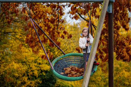 Happy child girl on swing in fall. Little kid playing in the autumn on playground, swinging and...