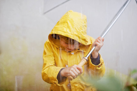 Beautiful little kid boy on way to school walking during sleet, heavy rain and snow with an umbrella on cold day. Happy and joyful child in colorful yellow coat fashion casual clothes.の写真素材