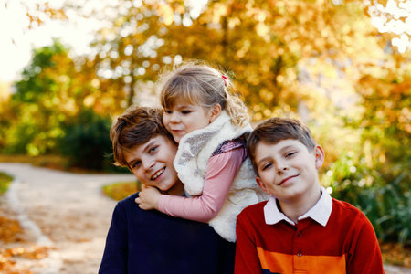 Portrait of three siblings children. Two kids brothers boys and little cute toddler sister girl having fun together in autumn park. Happy healthy family playing, walking, active leisure on natureの写真素材