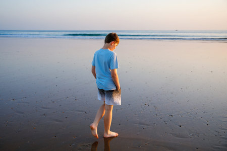 Happy cheerful teenager standing on beach at sunset. happy preteen boy smiling at the camera. Kid on...