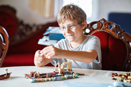 Little preschool or elementary school kid boy building a plastic blocks set at a table, focused and engaged in the activity. The scene is indoors, with a casual and warm atmosphere. Happy child.の写真素材