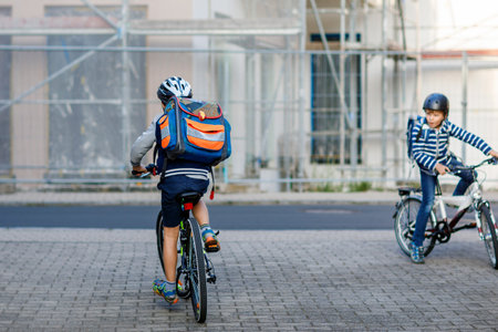 Two school kid boys in safety helmet riding with bike in the city with backpacks. Happy children in colorful clothes biking on bicycles on way to school. Safe way for kids outdoors to schoolの写真素材