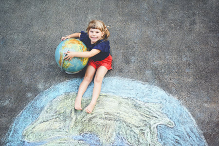 Little preschool girl with earth globe painting with colorful chalks on ground. Positive toddler child. Happy earth day concept. Creation of children for saving world, environment and ecology.の写真素材