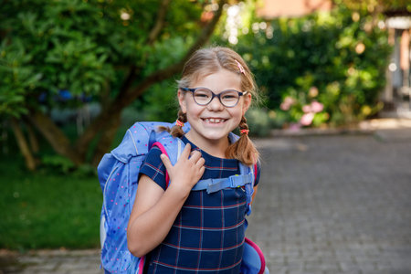 Happy little kid girl with eye glasses with backpack or satchel and big school bag on the first day...