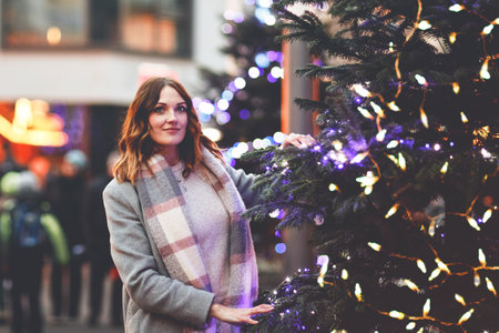 Beautiful young woman having fun on traditional Christmas market during strong snowfall. Happy girl enjoying traditional family market in Germany. Lady standing by illuminated xmas tree.の写真素材