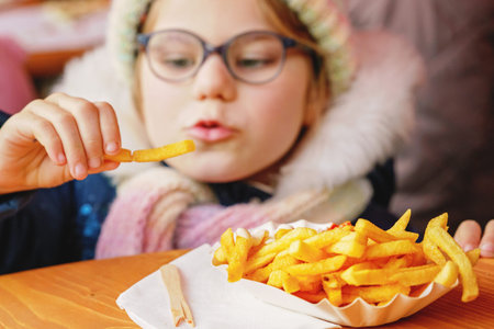 Portrait of happy smiling preschool girl eating french fries with tomato ketchup on Christmas market...