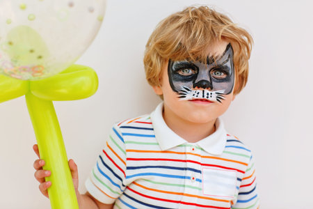 Beautiful little kid boy with face painted with animal or cat, on a birthday party. happy child...