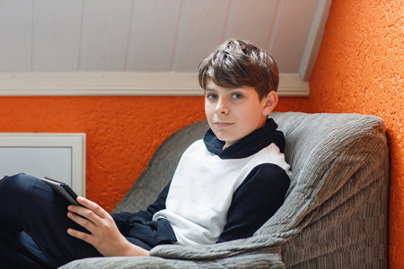 Teenager reading ebook reader at home. Happy teenage boy reads book on tablet, indoors.の写真素材