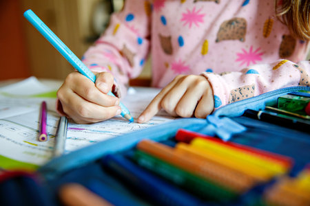Little girl making school homework. Cute child with eyeglasses learning at home, writing with pencils in workbook.の写真素材