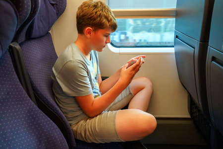 Cute adorable kid boy playing electronic games on tablet gadget during traveling by train. Happy child sitting near window. Family going on vacationsの写真素材