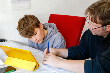 Happy father helping his son to do homework. Middle-aged man and teenage boy learning together for schoolの写真素材