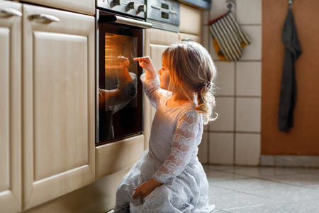 Cute blond girl baking muffins or pie in domestic kitchen. Happy toddler child having fun with helping, sitting near ofen and waiting for cookies. Kid baking for Thanksgiving or Christmas holiday.の写真素材