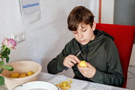 Teenager boy peeling potatoes in the kitchen. Teenage child helping with cooking and housework.の写真素材