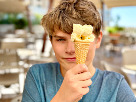 Cheerful laughing preteen boy eating multicolored ice cream in a waffle cone. Cool in the summer heat.Sweet snack for children. Happy child.の写真素材