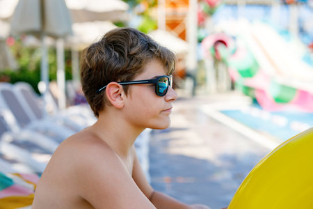 Cool school boy having fun on inflatable rubber circle in outdoor pool. Summer holiday. Summertime kids weekend. Child in swiming pool. Funny kid boy on ring at aquapark on family vacation.の写真素材