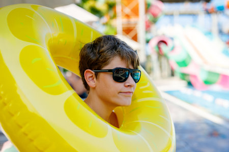 Cool school boy having fun on inflatable rubber circle in outdoor pool. Summer holiday. Summertime kids weekend. Child in swiming pool. Funny kid boy on ring at aquapark on family vacation.の写真素材