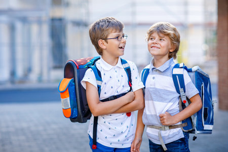 Two little kid boys with satchels. School kids on the way to school. Healthy children, brothers and best friends outdoors on the street leaving home. Back to school. Happy siblings.の写真素材