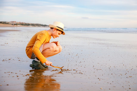 Happy cheerful teenager standing on beach at sunset. happy preteen boy smiling at the camera. Kid on...