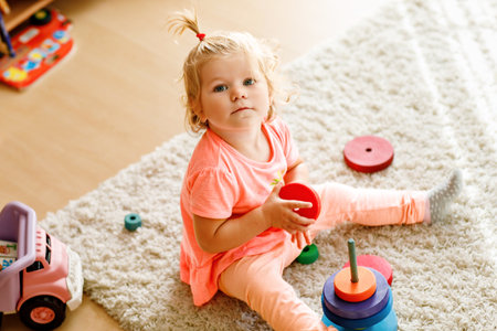 A child sits on a carpet, playing with colorful wooden rings and a toy truck, focused on stacking the pieces. The scene shows play with a rainbow colored pyramid at home.の写真素材