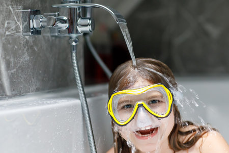 Litltle girl taking a bath with a foam in bathtub. Happy child having fun with swimming mask