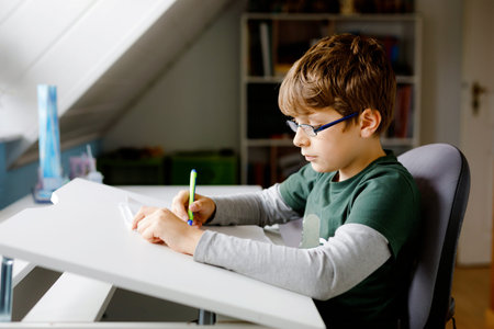Kid boy with glasses learns at home for school. Preteen child making homework.