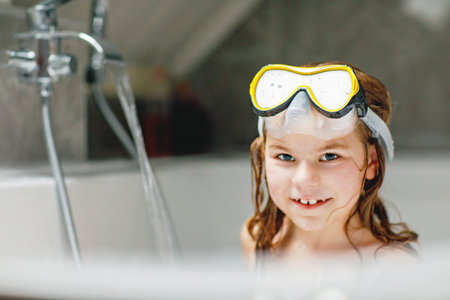 Litltle girl taking a bath with a foam in bathtub. Happy child having fun with swimming maskの写真素材