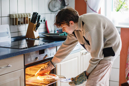 Handsome young teen boy baking pizza for lunch at home. Teenager holding Italian pizza
