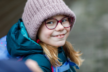 Cute little girl o the way to school. Healthy happy child with eyeglasses walking to primary school....