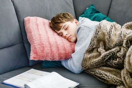 Tired Teenager sleep on the Sofa with the Books. School boy sleeps at homeの写真素材