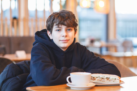 Teenager boy having breakfast in restaurant cafe. Happy teen boy eating stuffed bread and drinking coffee.の写真素材