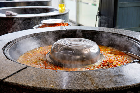 cooking traditional uzbek dish rice pilaf with meat lamb in a large cauldron in the kitchen of a...