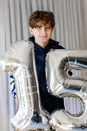 Portrait of happy teenager boy with air balloons with number 15 on his birthday. Smiling school...