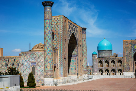 Registan Square in Samarkand, Uzbekistan, a historic architectural ensemble featuring three stunning madrasas with intricate mosaic designs, domes, and minarets under a bright blue skyの写真素材